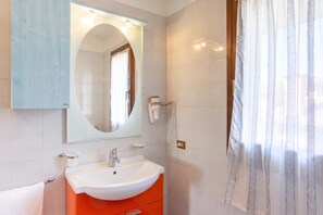 Un bagno con un lavandino bianco, uno specchio, una doccia e un telefono.