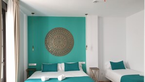 A hotel room with a bed, a smaller bed, teal and white bedding, a decorative wall hanging, and a small side table. - Dona Lola (Seville)