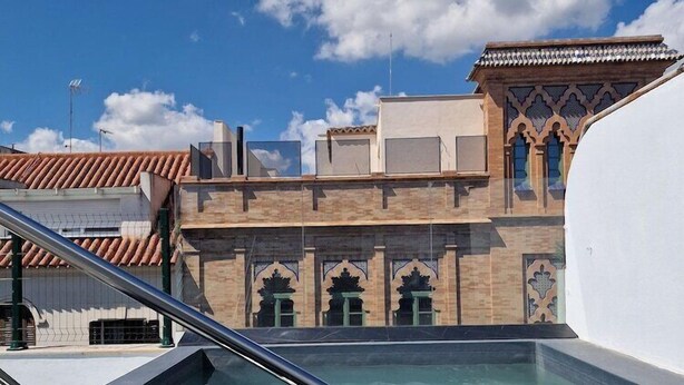 A swimming pool with a metal ladder, surrounded by buildings with traditional architecture and a clear blue sky. - Dona Lola (Seville)