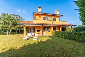 Una casa de dos pisos con un patio, mobiliario exterior y un césped bien cuidado.