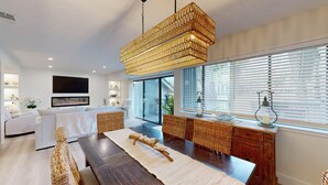 A modern living room with a large TV, comfortable seating, a dining area, and a large window with blinds. - Large Three Bedroom Villa Overlooking the George Fazio Golf Course! (Hilton Head)