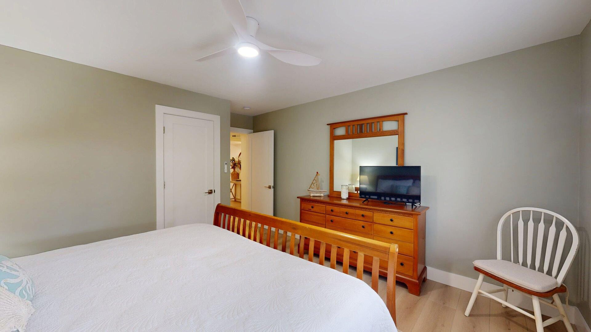 A bedroom with a bed, a dresser, a television, a chair, and a ceiling fan.