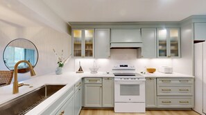 A modern kitchen with white countertops, a stainless steel sink, a white stove, and light blue cabinets.