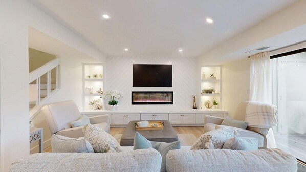 A modern living room with a fireplace, a flat-screen TV, and a staircase.
