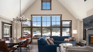 A spacious living area with a large window offering a mountain view, a cozy blue sofa, a dining table with chairs, and a fireplace.