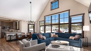 A spacious living room with a large sectional sofa, a coffee table, and a dining area with a kitchen in the background.