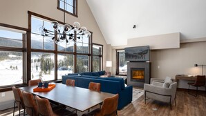 A spacious living room with a large window, a fireplace, and a dining area with a wooden table and chairs.