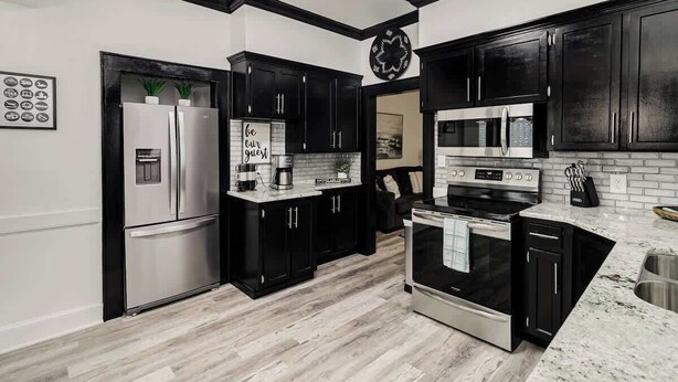 A modern kitchen with black cabinets, stainless steel appliances, and a marble countertop. - Historic Home Steps from Lake Hollingsworth, (Lakeland)