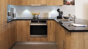 A modern kitchen with wooden cabinets, a stainless steel oven, and a black countertop.