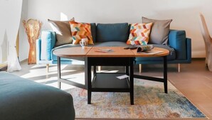 A modern living room with a blue sofa, colorful geometric pillows, a round coffee table, and a painting on the wall.