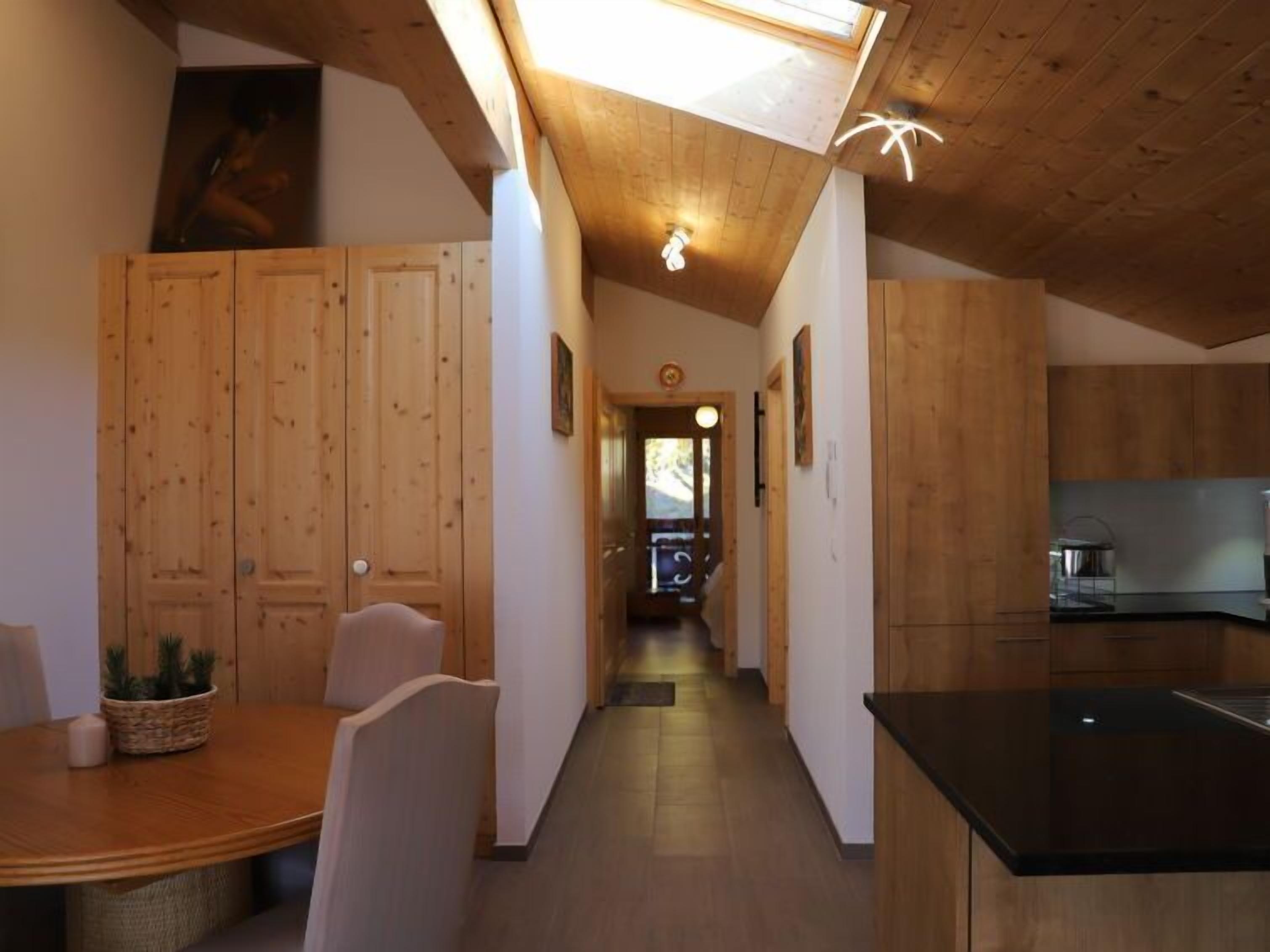 A wooden interior with a dining area, kitchen, and a hallway leading to a living space.