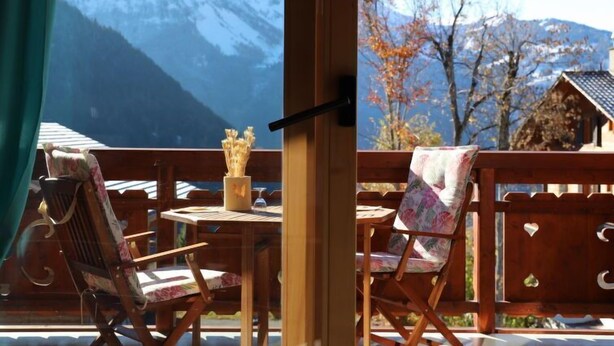 A wooden deck with two chairs and a table, overlooking a mountainous landscape.