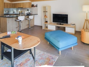 Ein modernes Wohnzimmer mit einem Holztisch, einem blauen Sofa, einem Fernseher und einer kleinen Holzkabine.