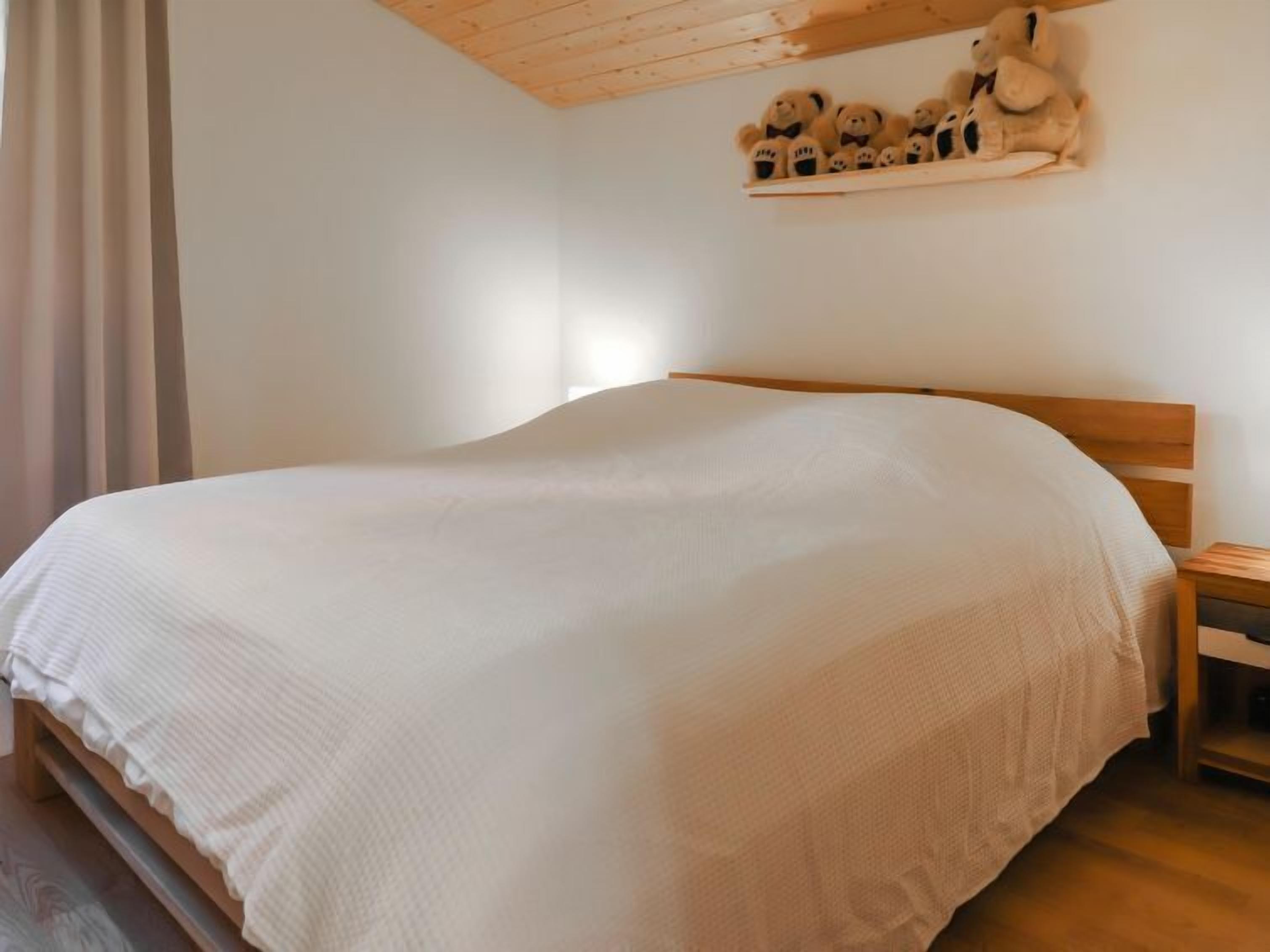 A neatly made bed with a wooden headboard, a bedside table, and a shelf with teddy bears.