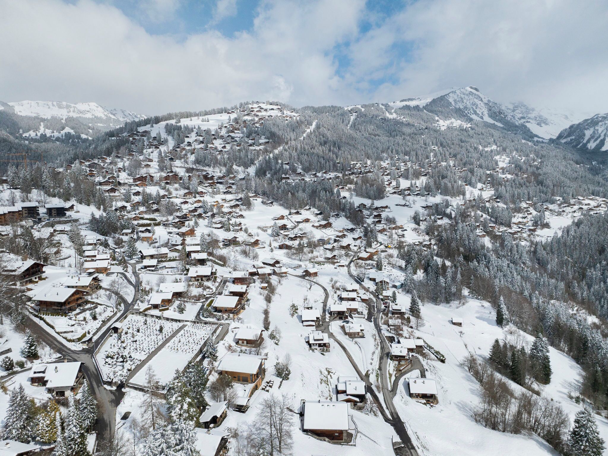 Un pueblo cubierto de nieve con casas de madera tradicionales, carreteras serpenteantes y montañas al fondo.