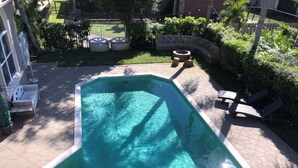 Una piscina con borde de baldosas, rodeada por un muro de piedra y vegetación.