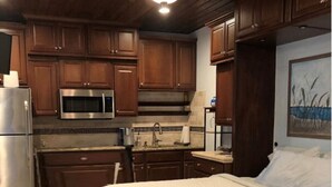 Un dormitorio con cama, mesita de noche, una mesa azul y una kitchenette equipada con refrigerador, microondas y lavaplatos.