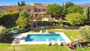 Una piscina con sillas de descanso, un muro de piedra y una casa grande con techo de tejas.