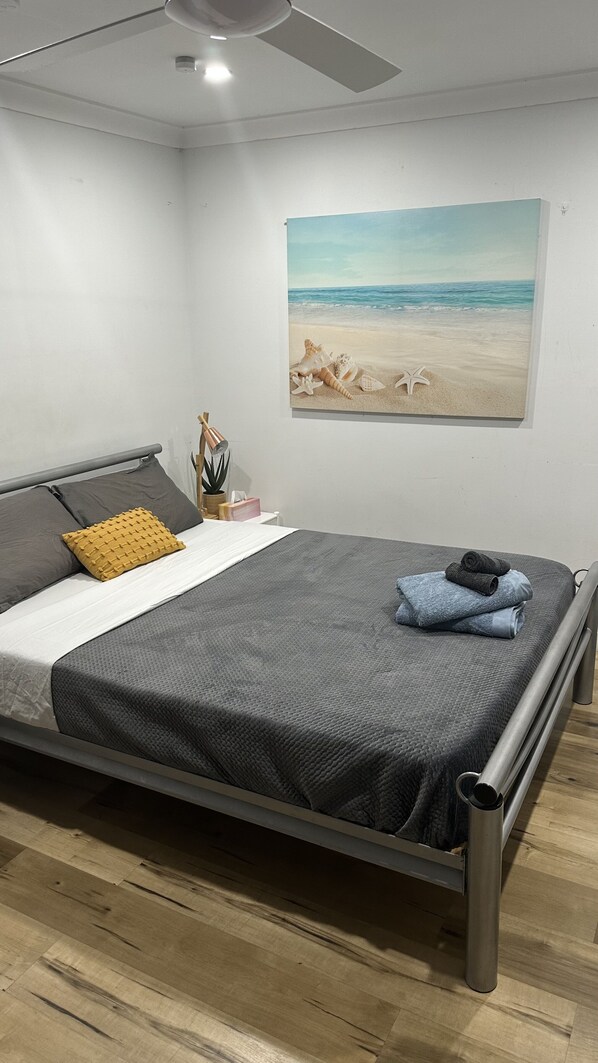 A modern bedroom with a bed, a painting of a beach, and a ceiling fan. - Cosy Private Studio / Hotel style in Five Dock (Five Dock)