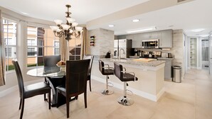 Een moderne keuken met een centraal eiland, barstoelen en een eethoek met een glazen tafel en stoelen.