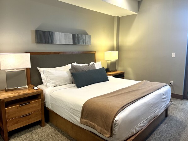 A neatly made bed with a brown throw blanket, two bedside tables with lamps, a wooden nightstand, and a wall-mounted artwork. - True Ski-in Ski-out - 2BR, sleeps 8, ONLY New Year Week (Breckenridge)