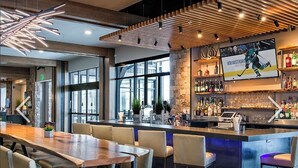 Zona de bar moderna con barra de madera, asientos con sillas acolchadas y un amplio ventanal que proporciona luz natural.