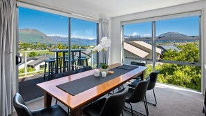 A hotel room with a large window offering a mountain view, a wooden table with chairs, and a small potted plant. - Kings View - Wanaka Holiday Home (Wanaka)