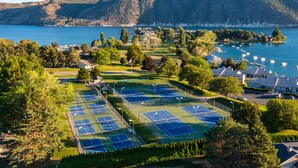 Complejo de canchas de tenis con varias pistas, rodeado de árboles y vistas a un lago.