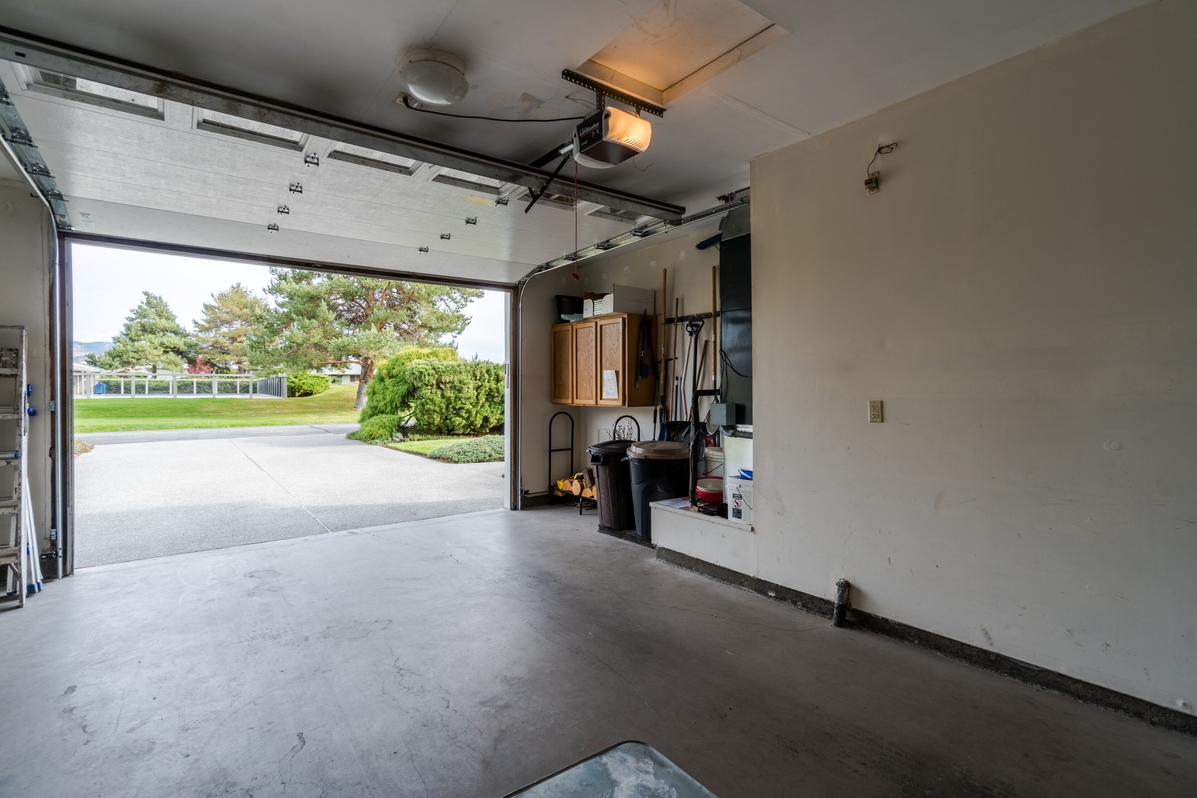 A garage with a concrete floor, a ceiling-mounted projector, and a view of a residential area with trees and a house.