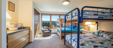 Une chambre avec des lits superposés, un bureau avec des tiroirs, une chaise, une lampe et une fenêtre donnant sur un beau paysage.