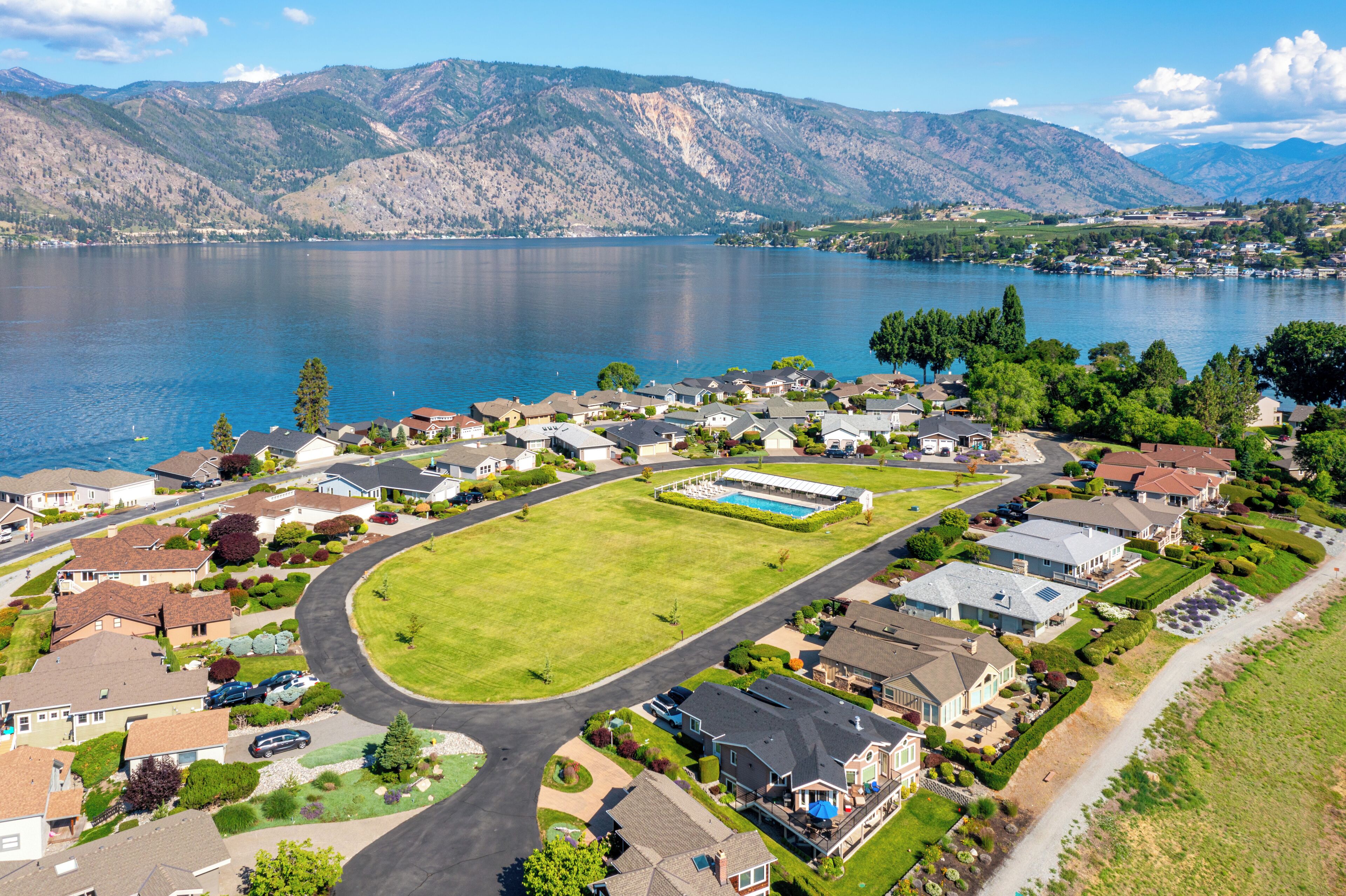 A residential area with houses, a swimming pool, and a lake with mountains in the background.