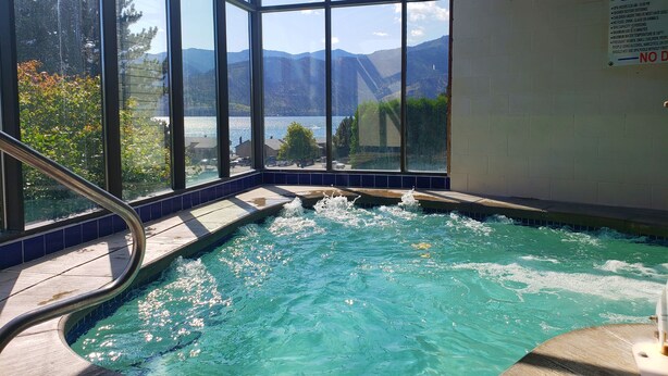Un jacuzzi con recinto de vidrio, con vistas a montañas y un lago.