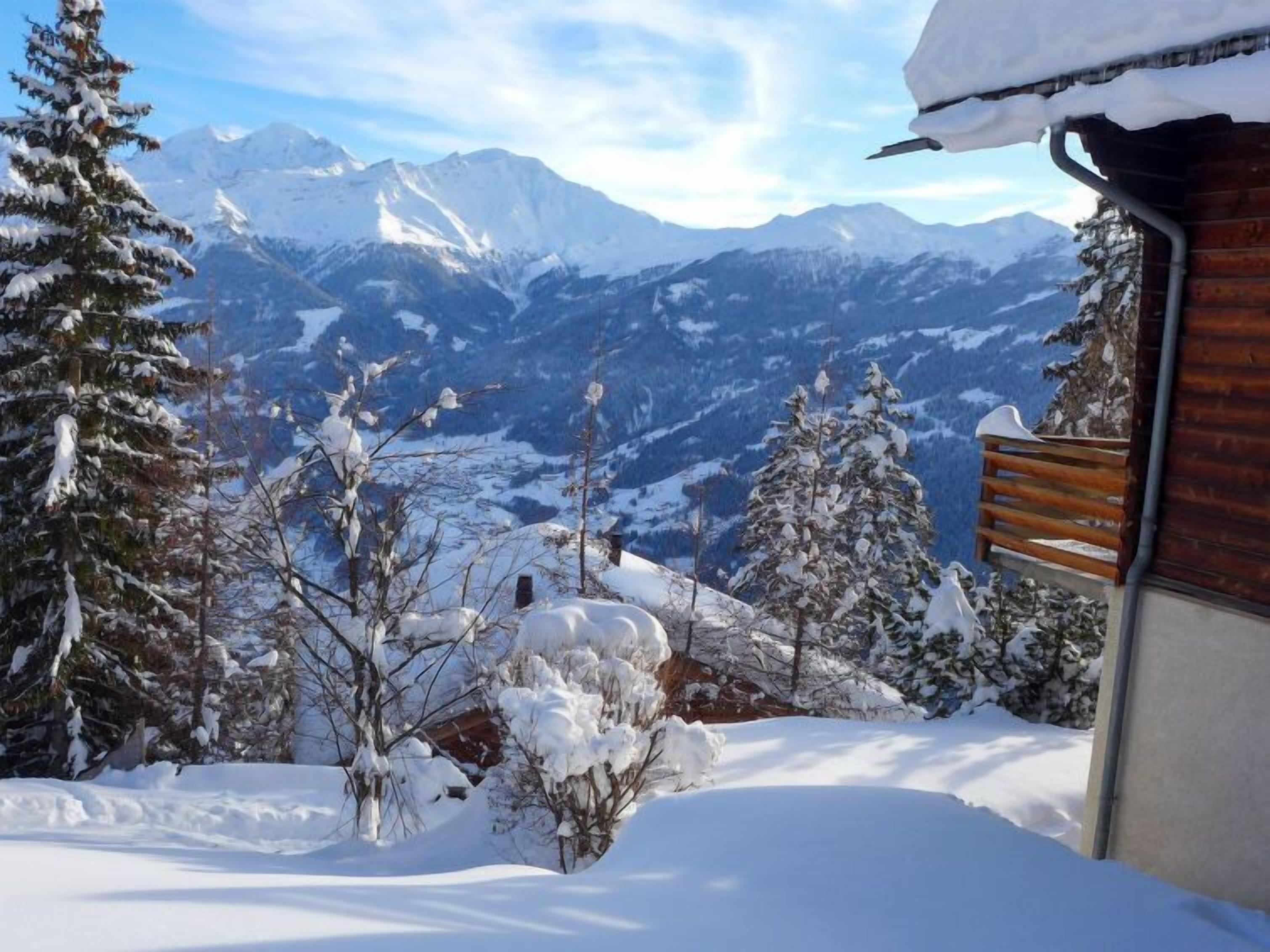 Un paysage de montagne enneigé avec une cabane en bois et des arbres couverts de neige.