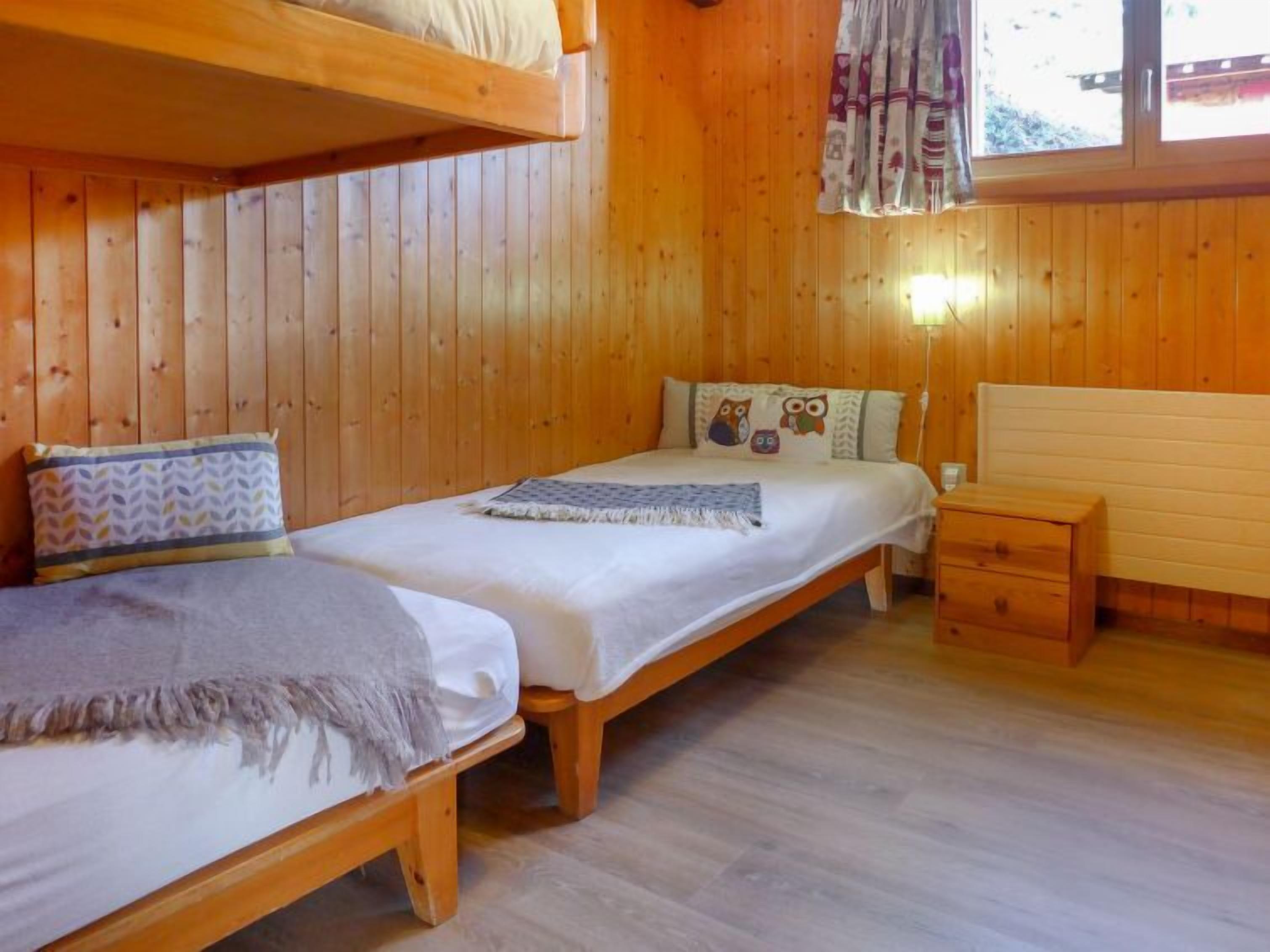 Habitación de cabaña de madera con dos camas individuales, una mesita de noche y una ventana con cortinas.