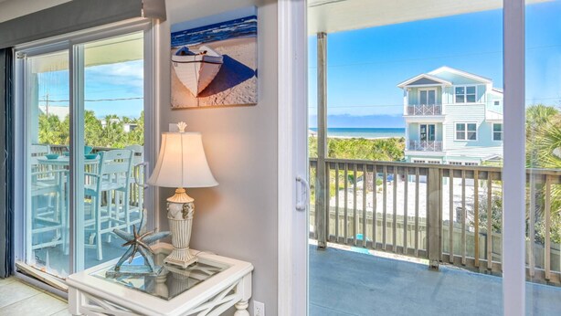Un balcon avec une table, des chaises, une lampe et un tableau représentant une scène de plage.
