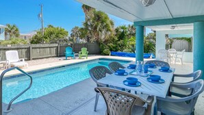 Un espace aménagé au bord de la piscine, avec une table dressée pour les repas, des chaises et un coin salon abrité.