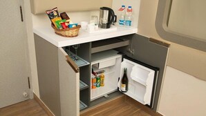 A compact kitchenette with a refrigerator, a coffee maker, and a small countertop with snacks and drinks. - Ramyas Hotels (Tiruchirappalli)