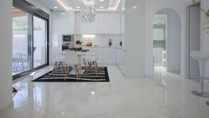Una cucina moderna con mobili bianchi, un'area pranzo con tappeto bianco e nero e un'ampia finestra che offre luce naturale.