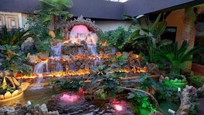 Un giardino curato con un elemento centrale d'acqua, tra cui una cascata e uno stagno, circondato da piante e rocce di varie tipologie.