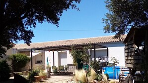 A courtyard with a tiled-roof building, potted plants, a bicycle, and outdoor furniture. - Bed and breakfast, quiet area near Orange, Vaucluse (Sérignan-du-Comtat)