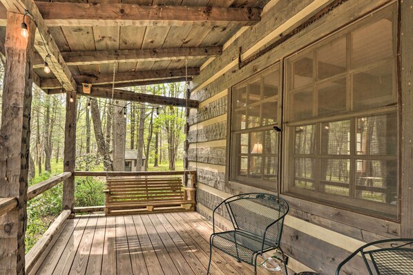Una terraza de madera con un banco y sillas, ventanas amplias y vistas al bosque.