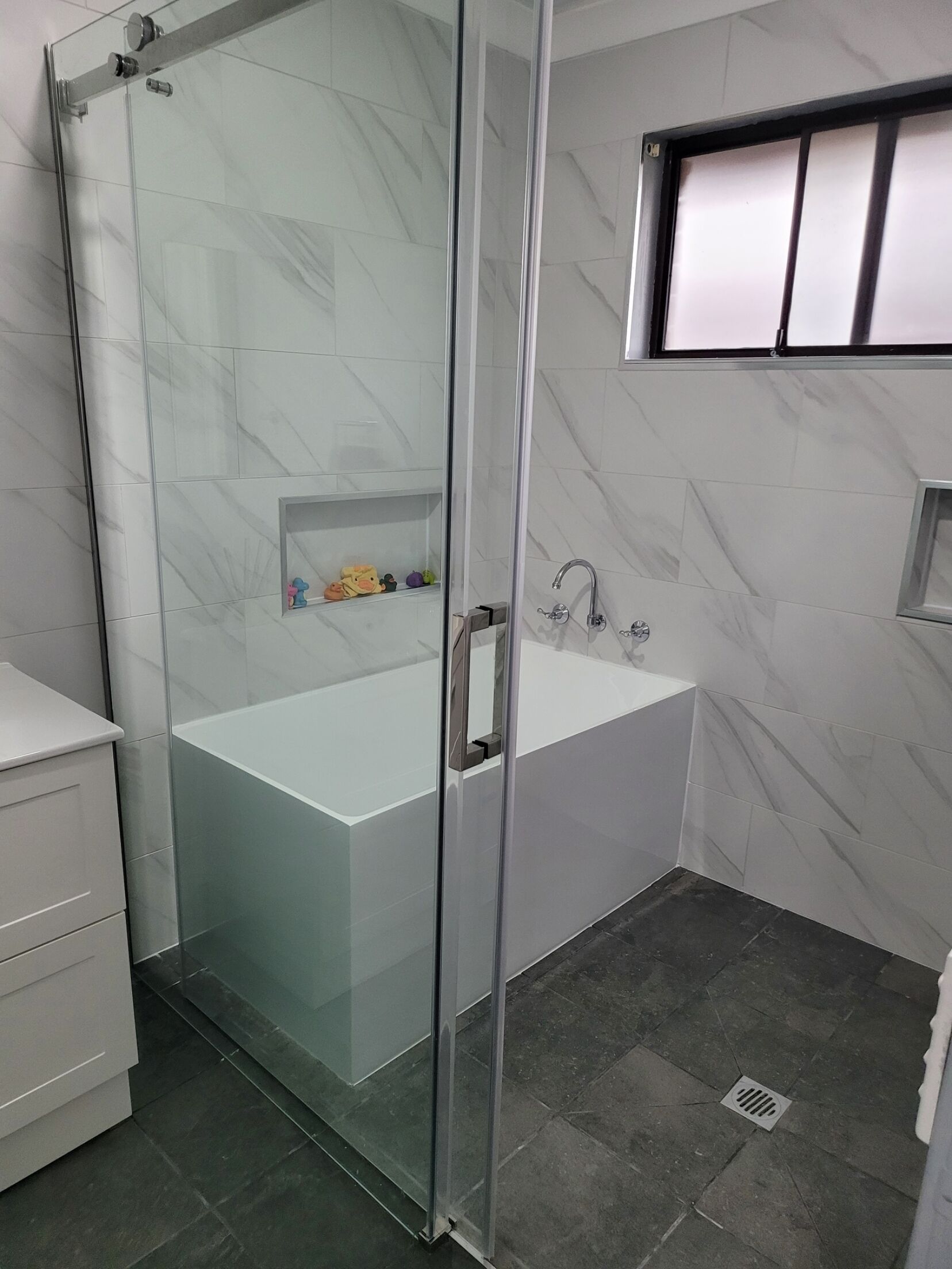 A modern bathroom with a glass-enclosed shower, a white bathtub, and a marble-tiled wall.