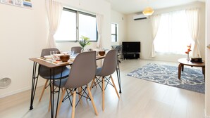 Ein modernes Wohnzimmer mit Essbereich, inklusive Flachbildfernseher, Esstisch mit Stühlen und einem blau gemusterten Teppich.