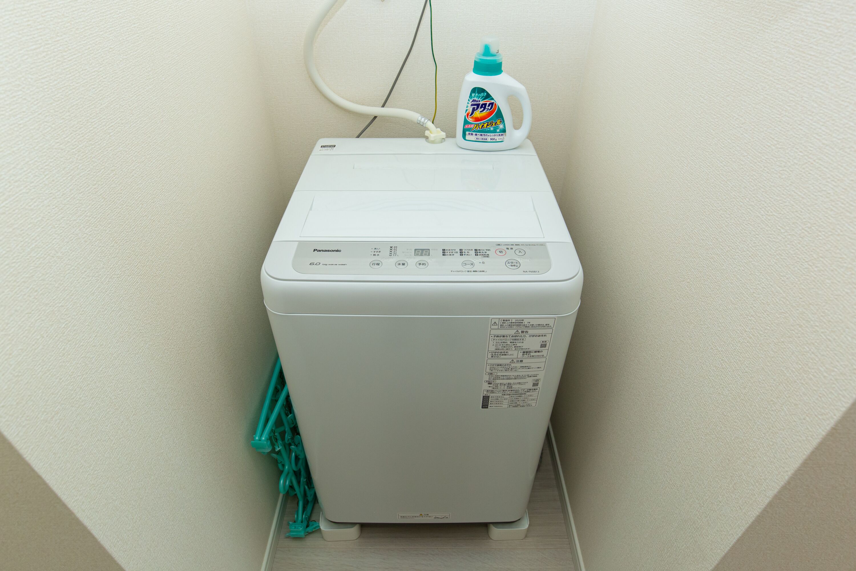 A white washing machine with a detergent bottle on top, connected to a power outlet.