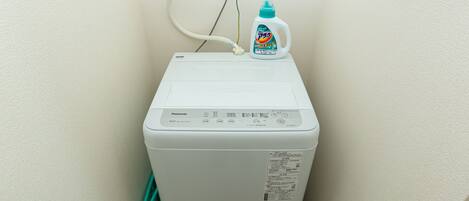 Lavadora blanca con una botella de detergente encima, conectada a un enchufe.