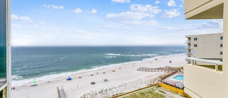 Vista sulla spiaggia dal balcone di un appartamento, con spiaggia sabbiosa, piscina e terrazza in legno.