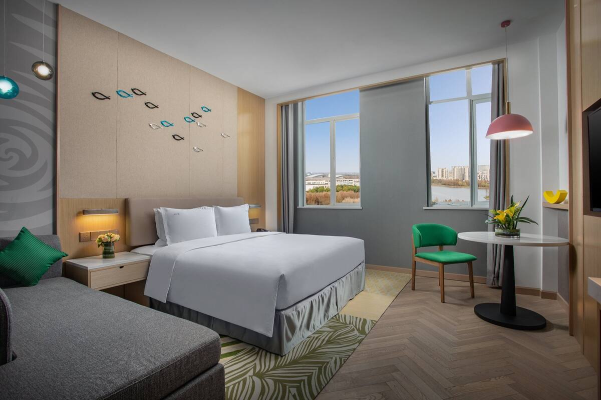 Ett modernt hotellrum med en stor säng, ett skrivbord, en stol och utsikt över staden.