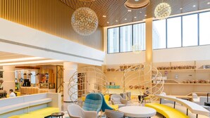 Eine geräumige Lobby mit moderner Sitzgelegenheiten, einem großen Fenster und dekorativen, kugelförmigen Leuchten.