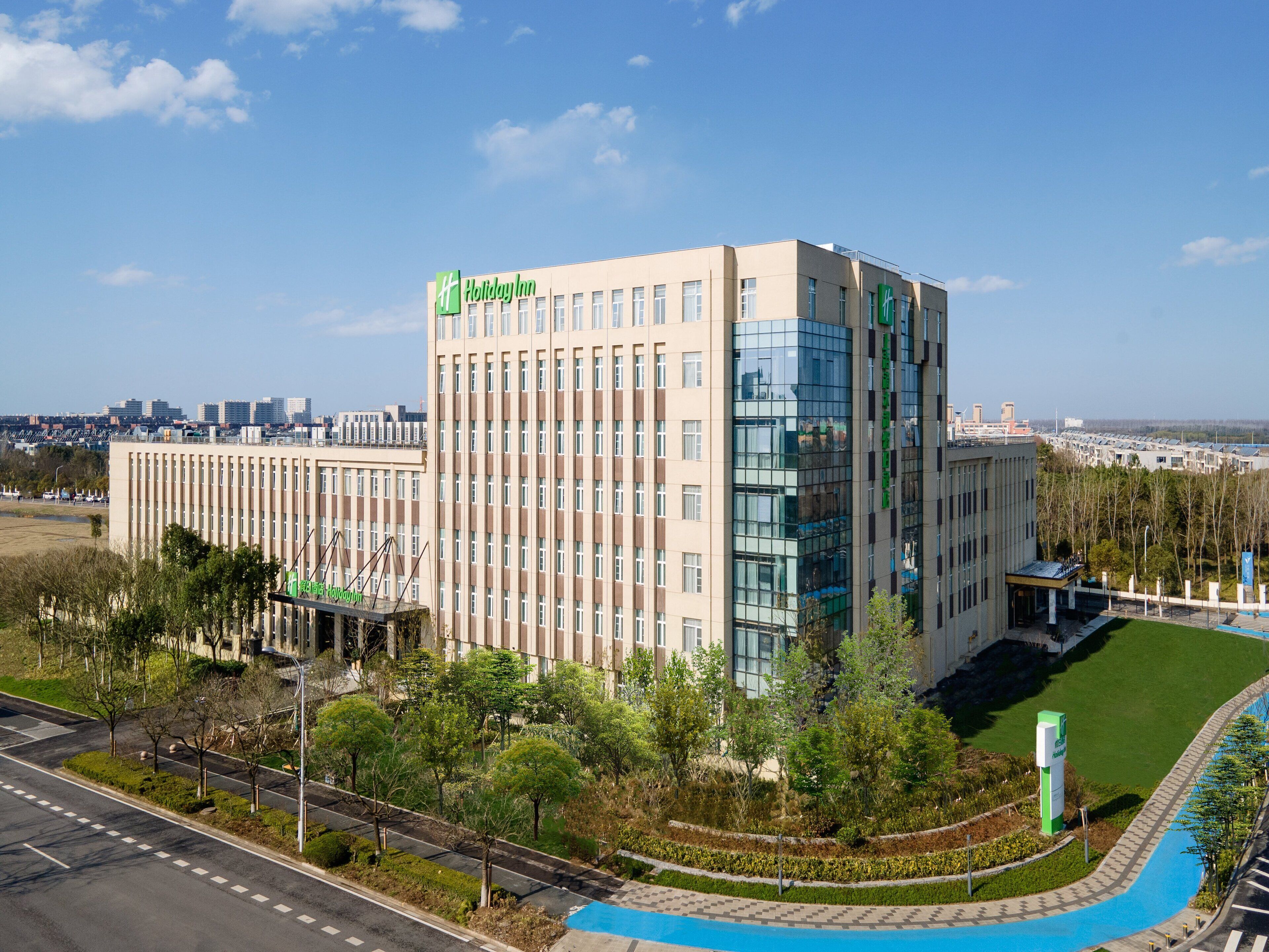 Ein Hotel Holiday Inn mit modernem Design, das Glas- und Backsteinfassaden kombiniert und von Grünflächen sowie einem blauen Weg umgeben ist.