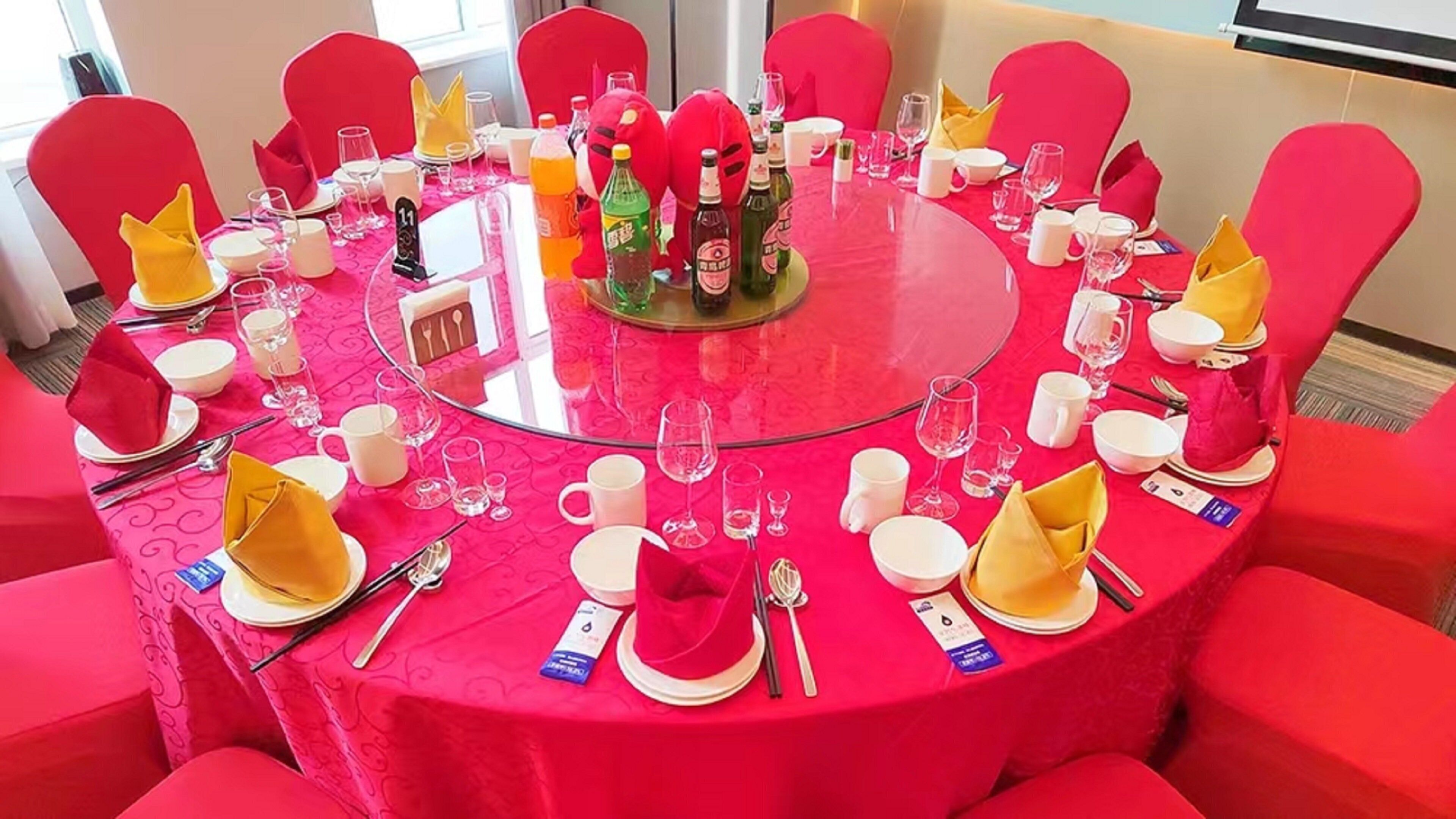 A round table with a glass top, surrounded by red chairs, set with plates, glasses, and cutlery.